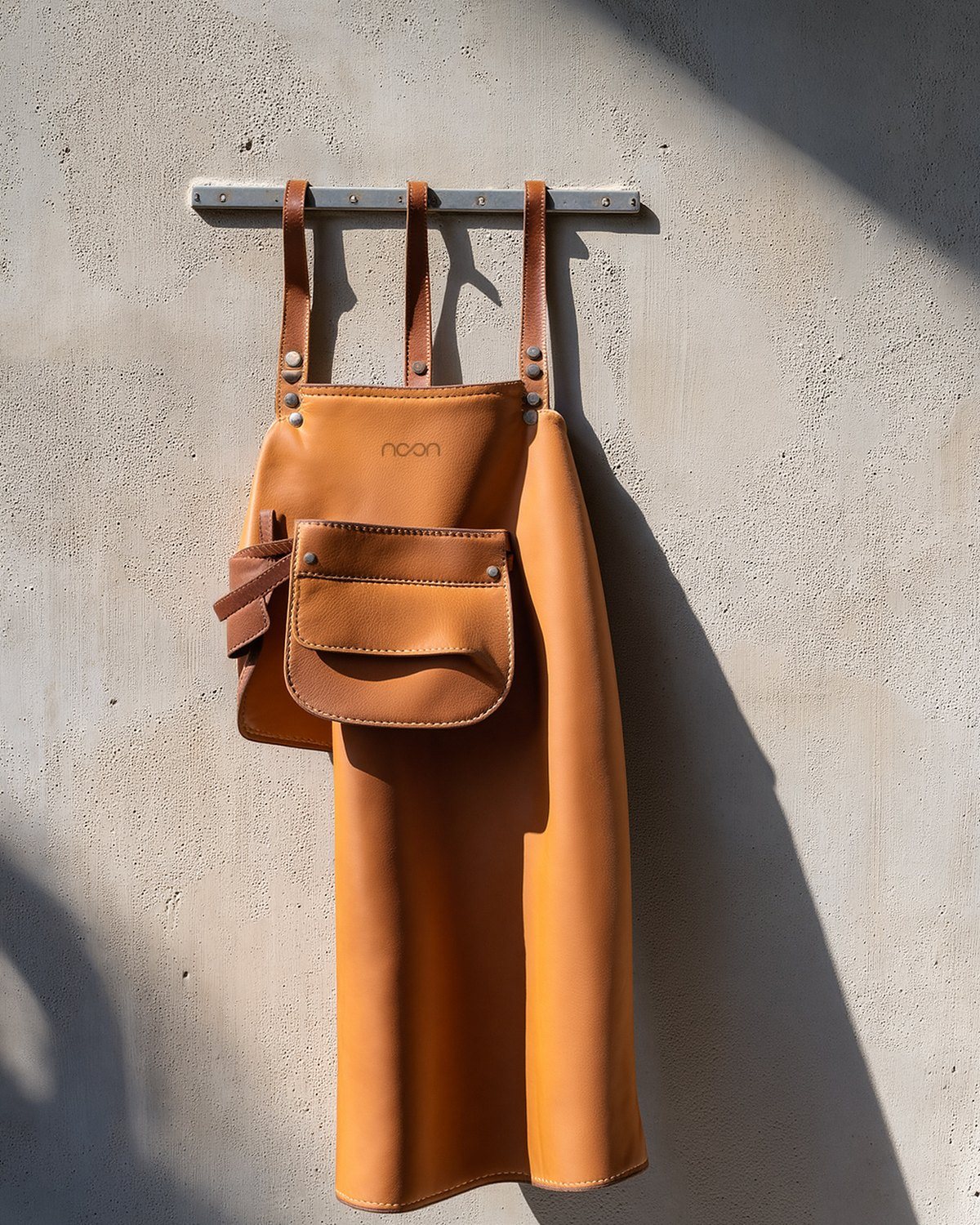 A tan leather apron with a pouch, the word noon stamped small at the bib