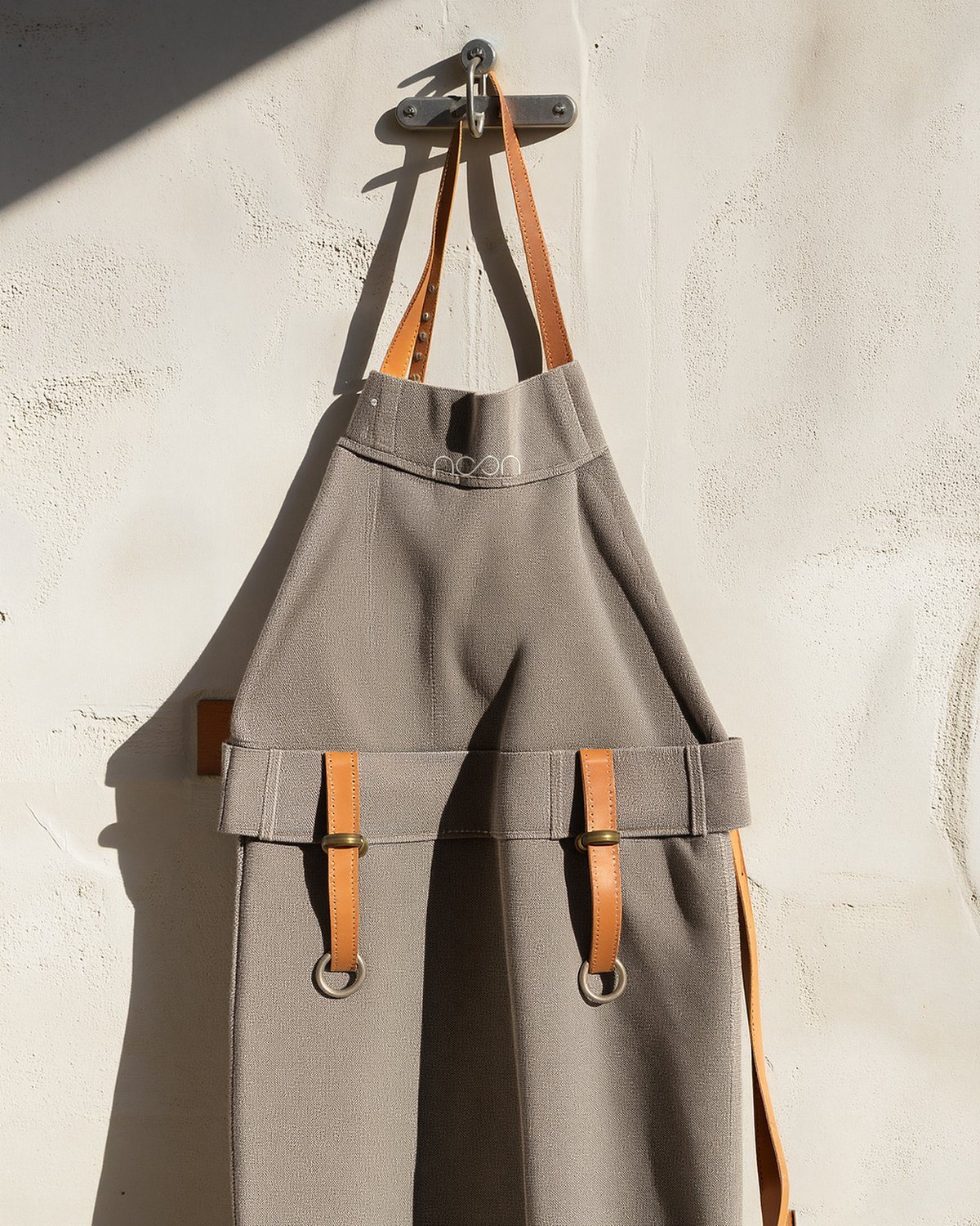 A grey canvas apron with tan leather straps and brass rings