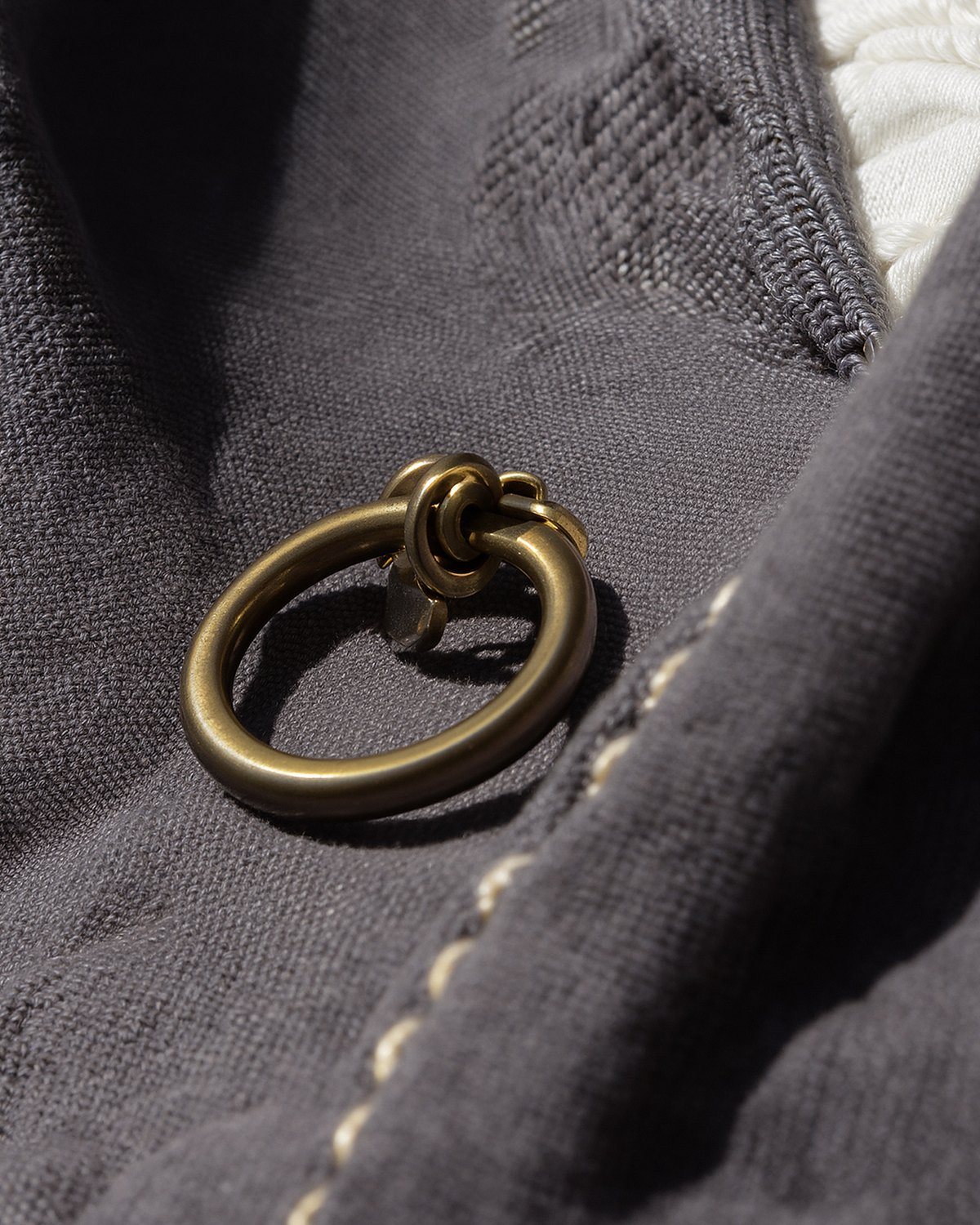A brass ring on dark grey cloth beside a line of limestone saddle stitch, close up