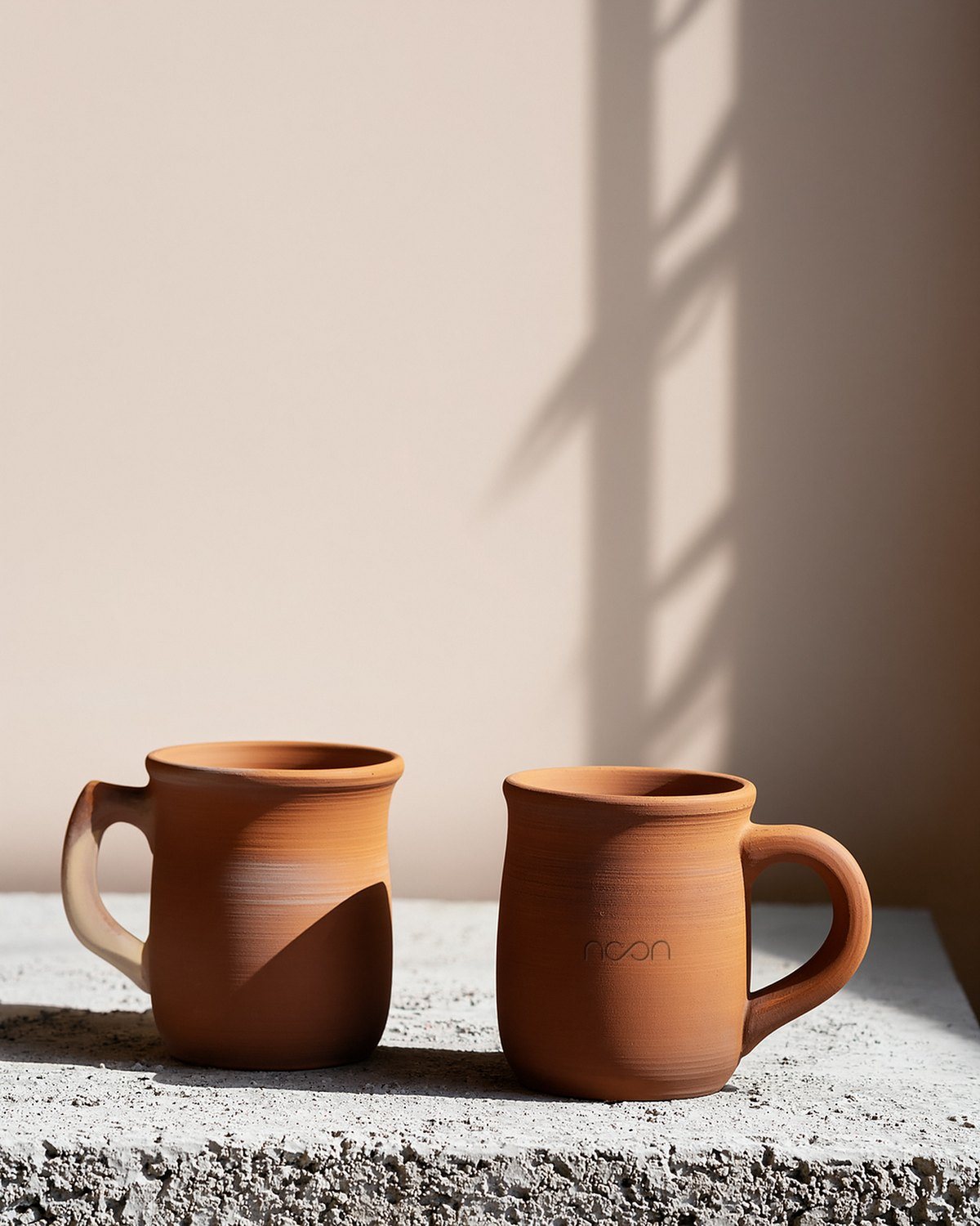 Two small terracotta mugs on a ledge against a plaster wall, the word pressed into one