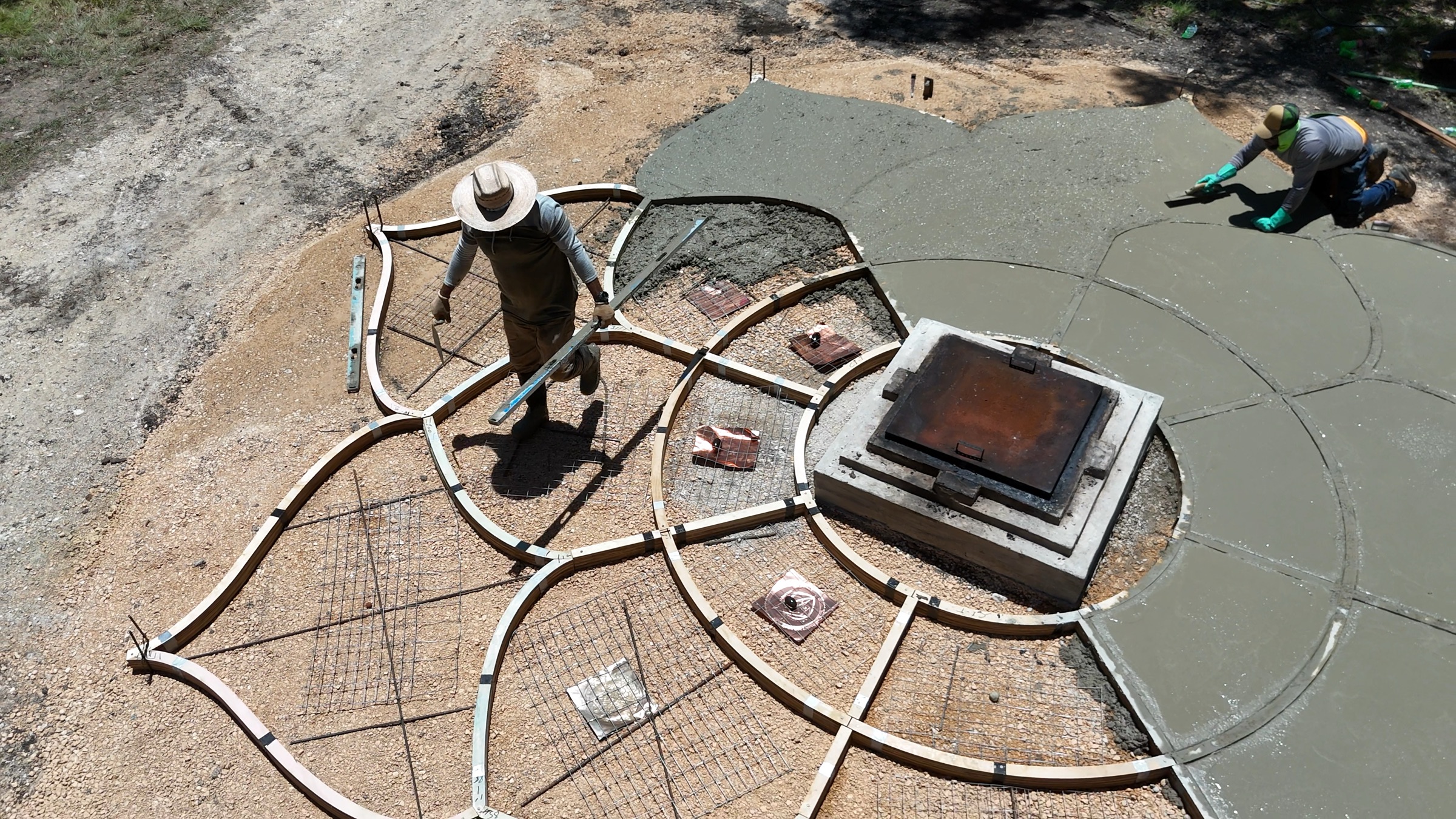 Drone view of the crew pouring The Lotus: birch petal forms on one side, fresh concrete on the other.