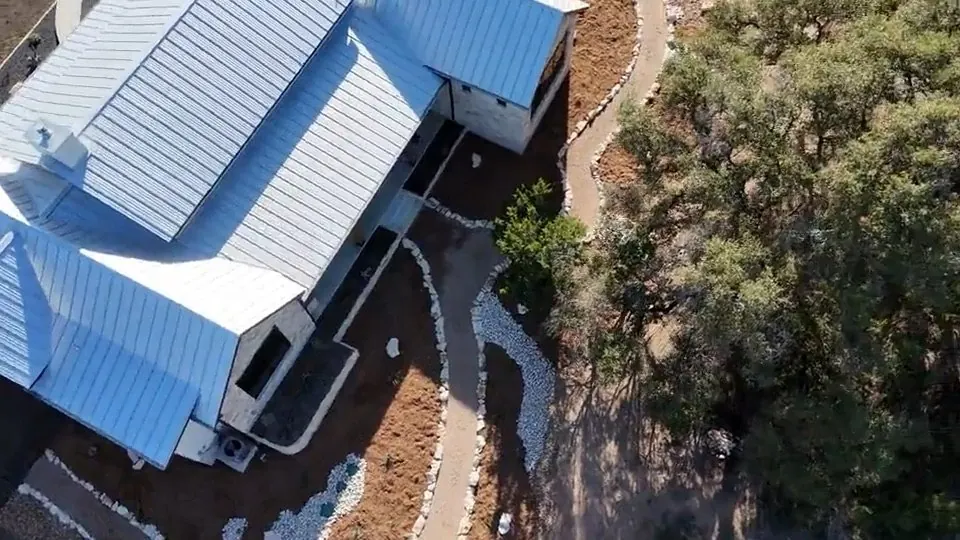 A dry creek of river rock seen from above, carrying roof water away from a house.