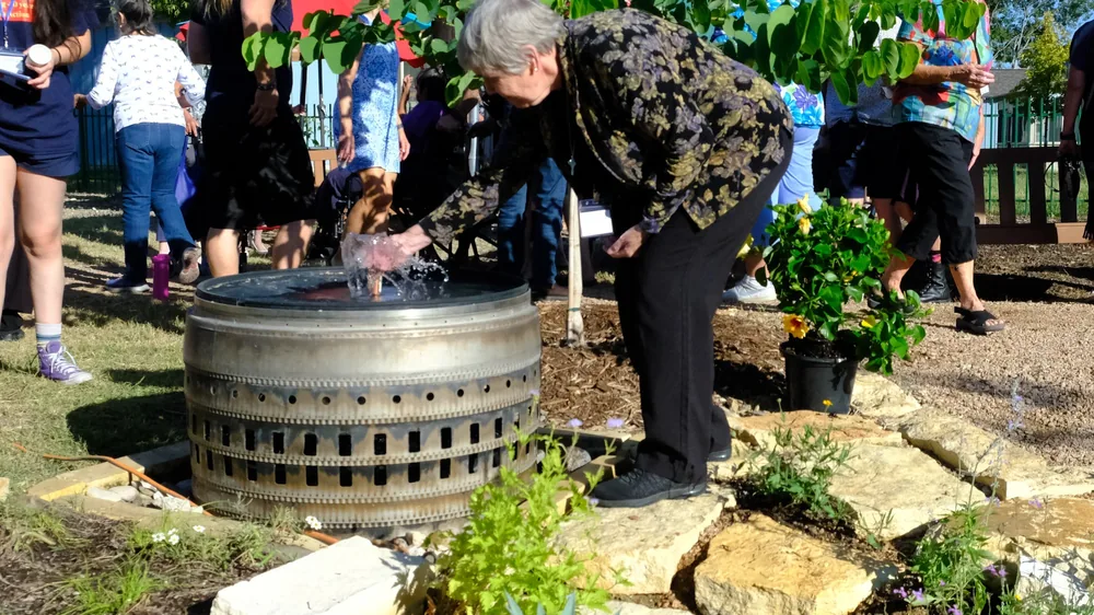A resident reaches into the jet of the cast basin at Towne Twin on planting day, the crowd behind her.