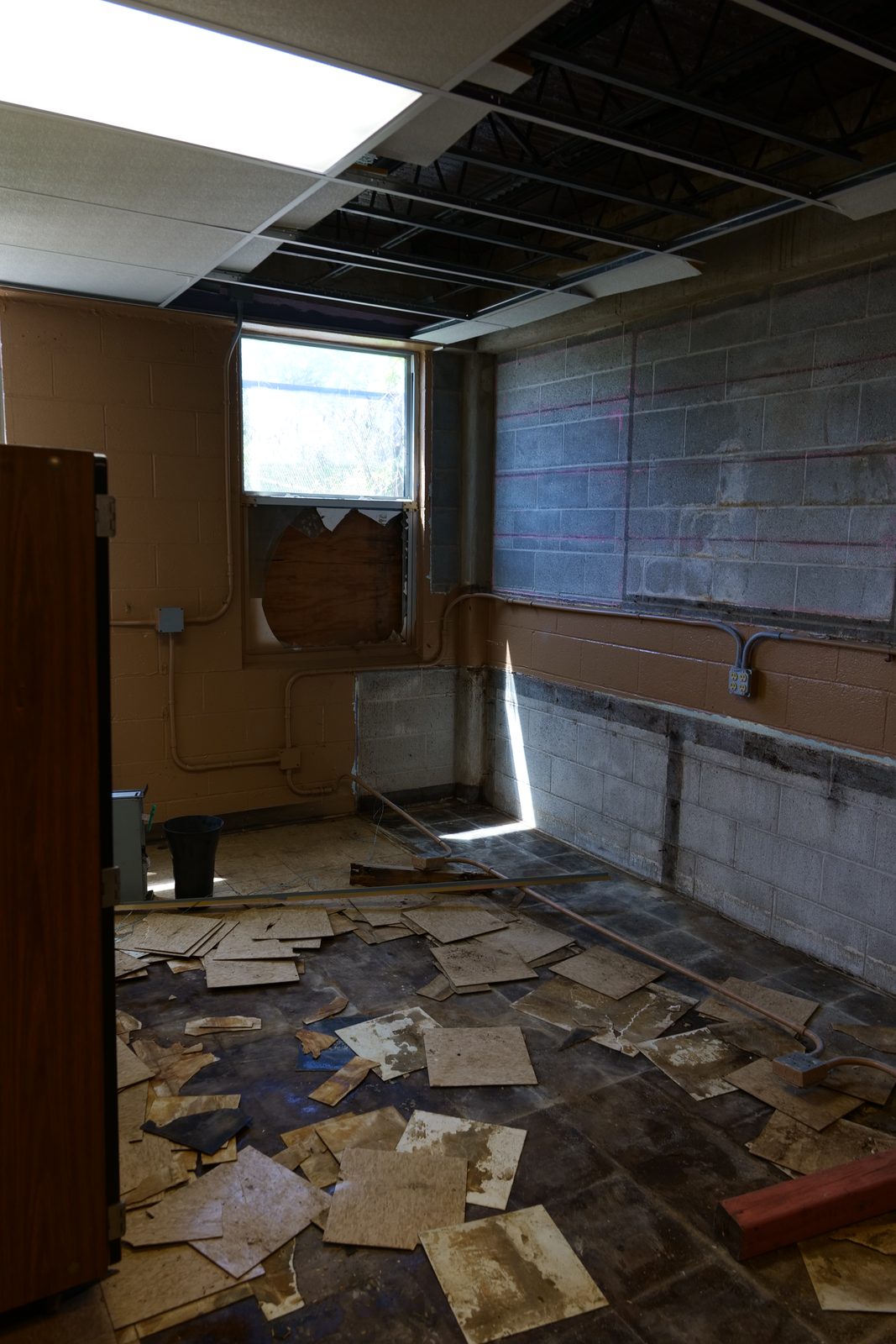 A gutted room at 702 — the drop ceiling torn out to the steel deck, ceiling tiles strewn across a water-stained floor.