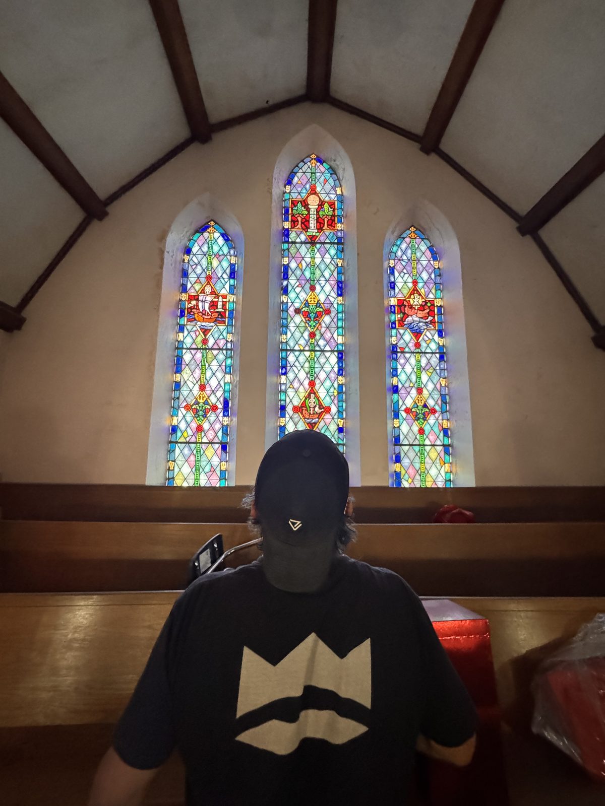 A person standing quietly before the three restored stained-glass windows inside 702, back to the camera.