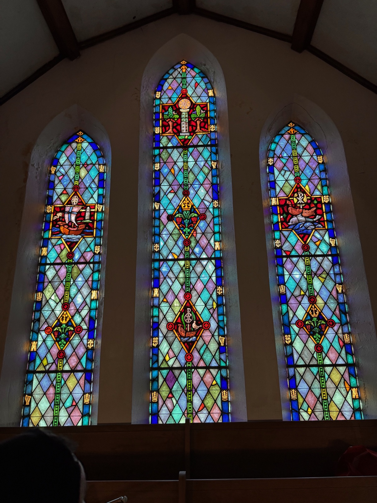 A stained-glass triptych of three tall Gothic arched windows inside 702, lit from outside.