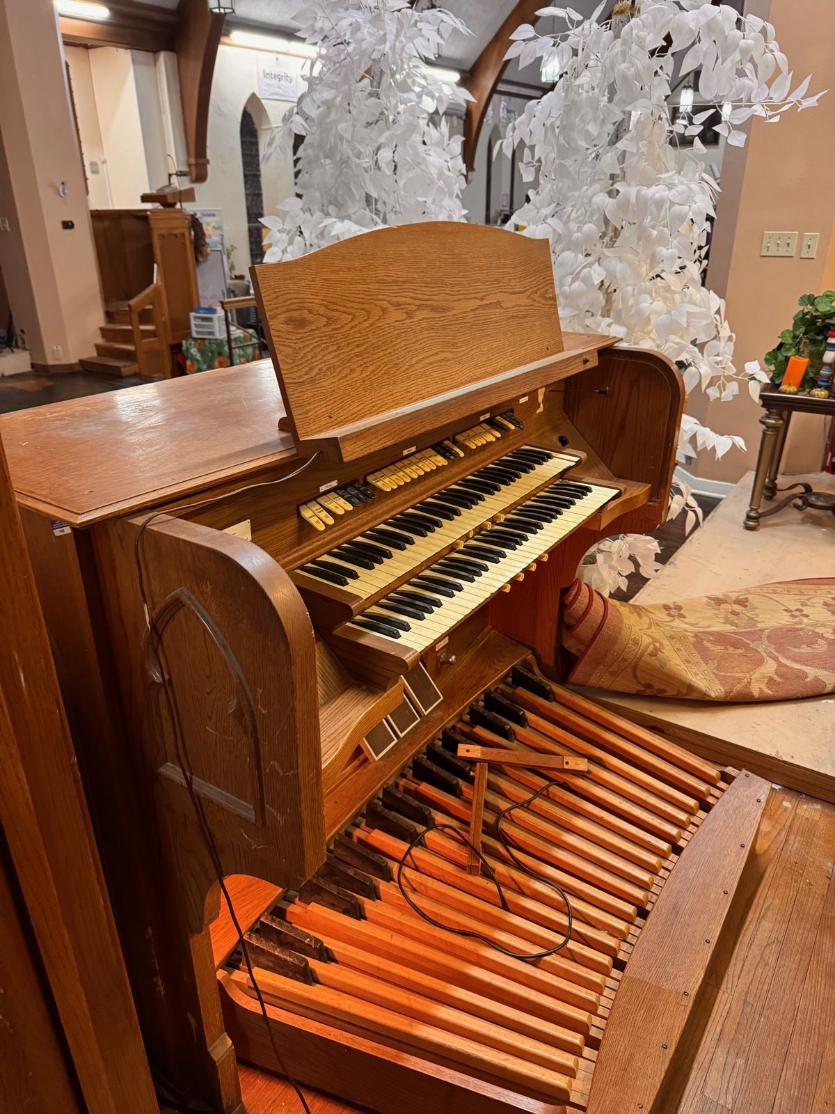 The pipe organ inside 702 — oak console and pedalboard intact, white blossoms cascading above it.