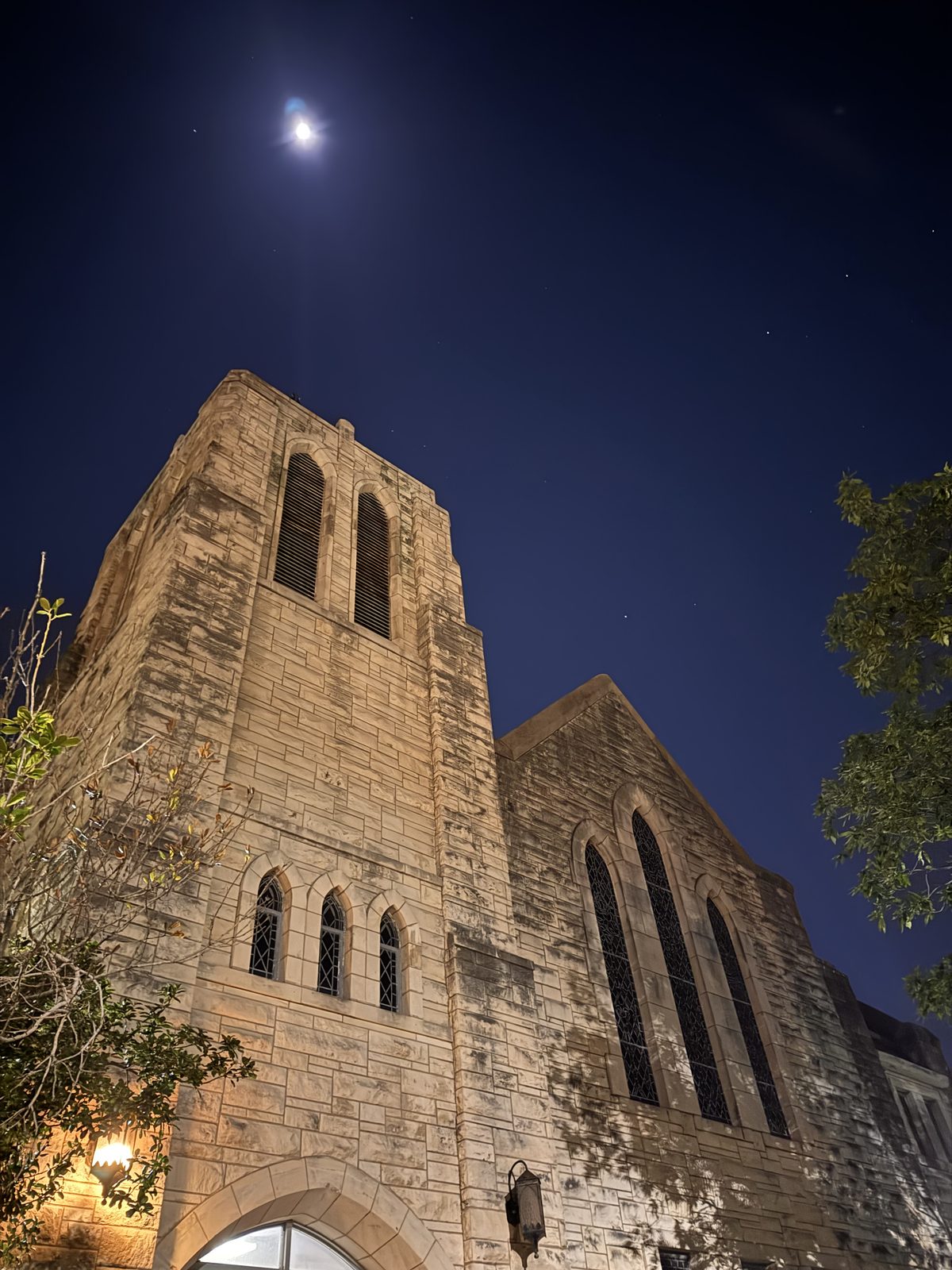 The stone bell tower of 702 rising into a deep blue night sky, the moon above it.