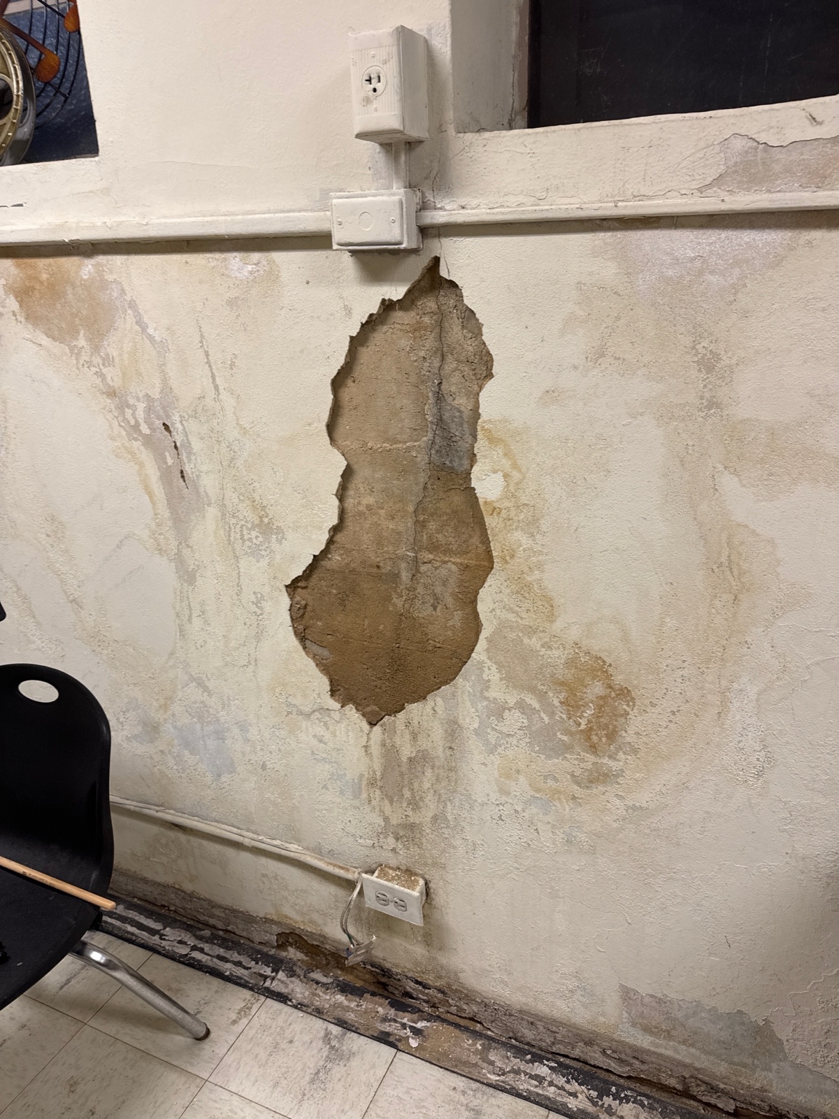 An interior wall with plaster fallen away, water staining, and a dangling outlet.