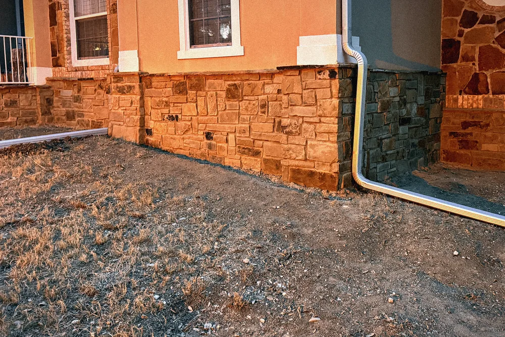 The finished limestone skirt along a stucco foundation at dusk: coursed cut stone under the windows, lit warm by the low sun.