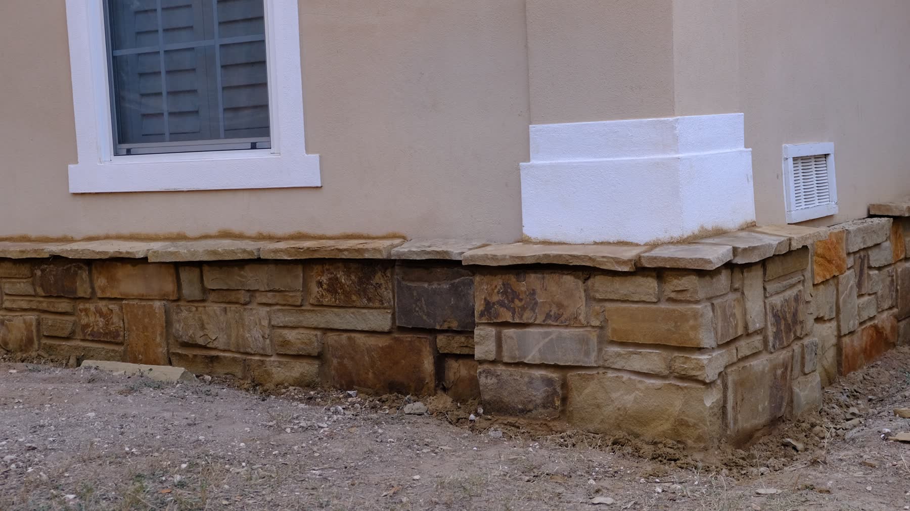 A finished stone-veneer foundation retrofit in warm Hill Country limestone against tan stucco.
