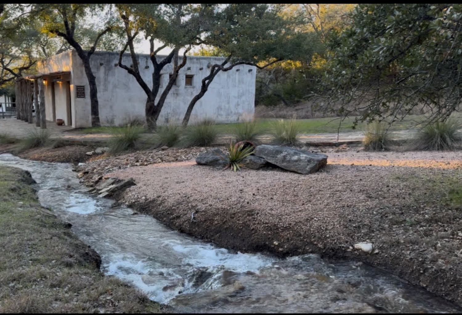 A small water channel running through the grounds toward a mission-styled building at golden hour.