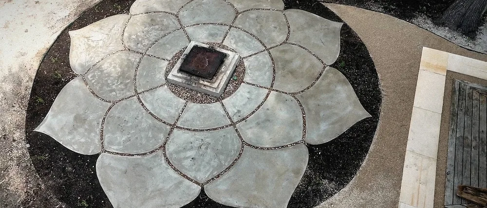 The finished Lotus low and wide: eight cast petals with pebble joints around the square plinth, the pavilion's plaza at the edge.