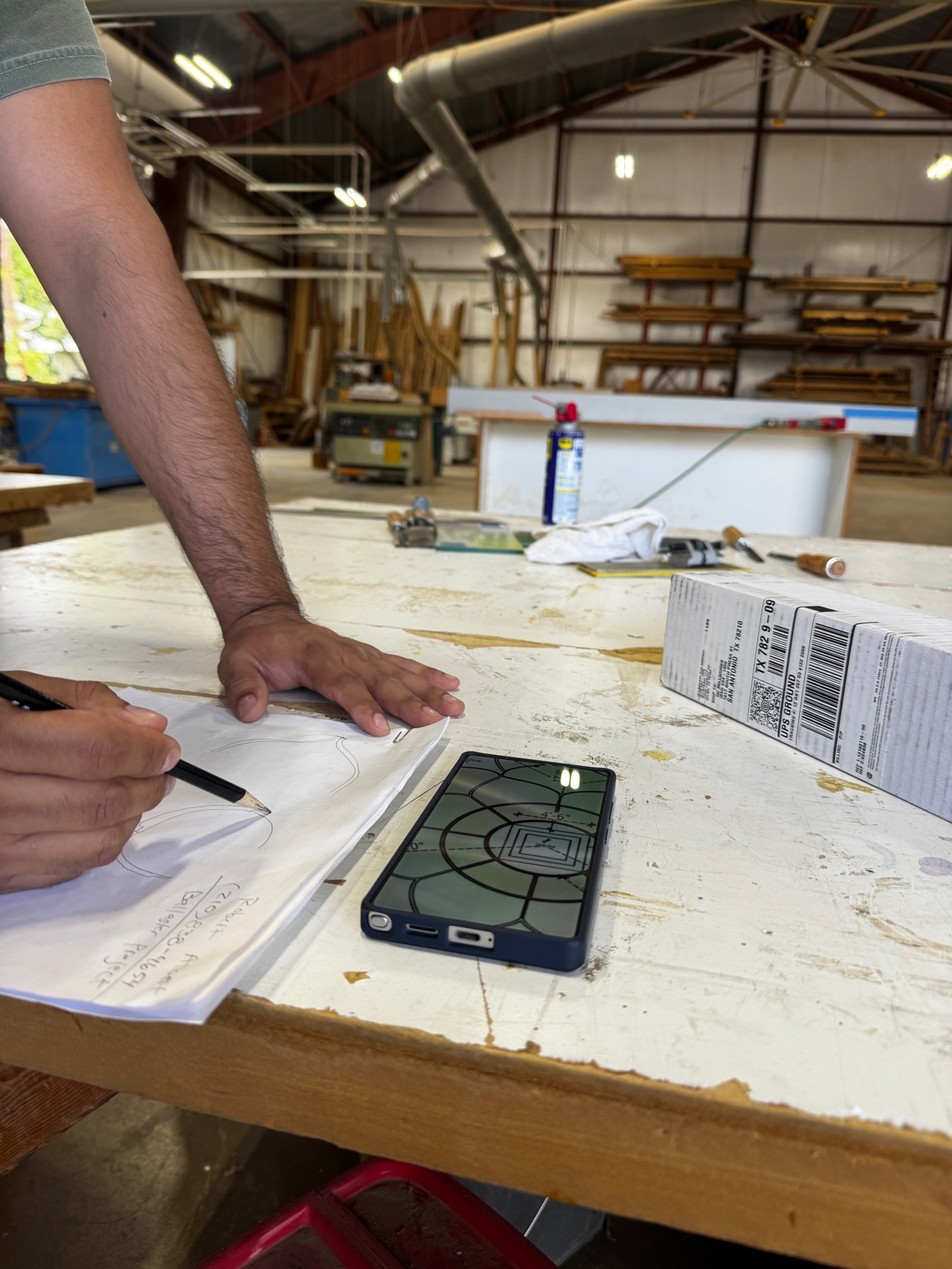 Hands sketching the lotus geometry on paper at a workshop table, a phone showing the CAD render alongside.