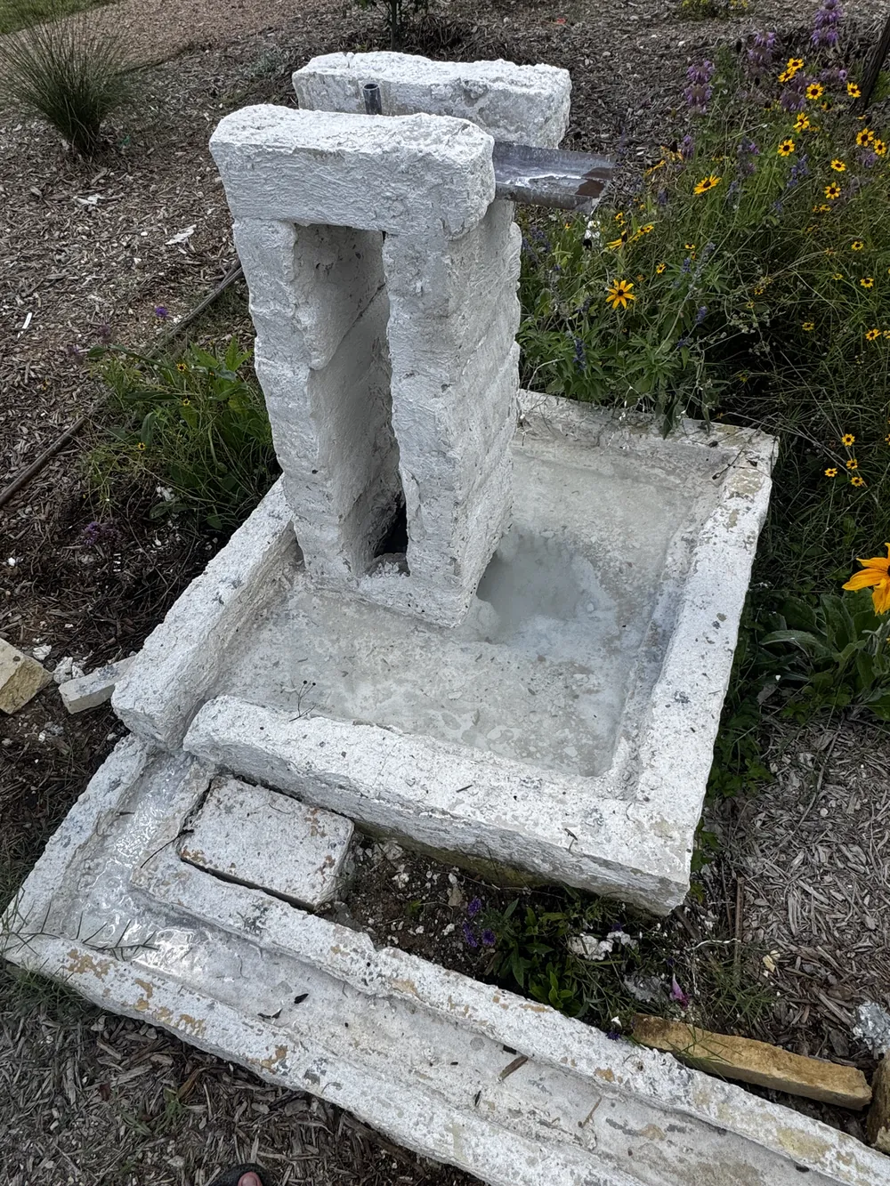 The cast concrete fountain standing among blanketflowers beside the rill.