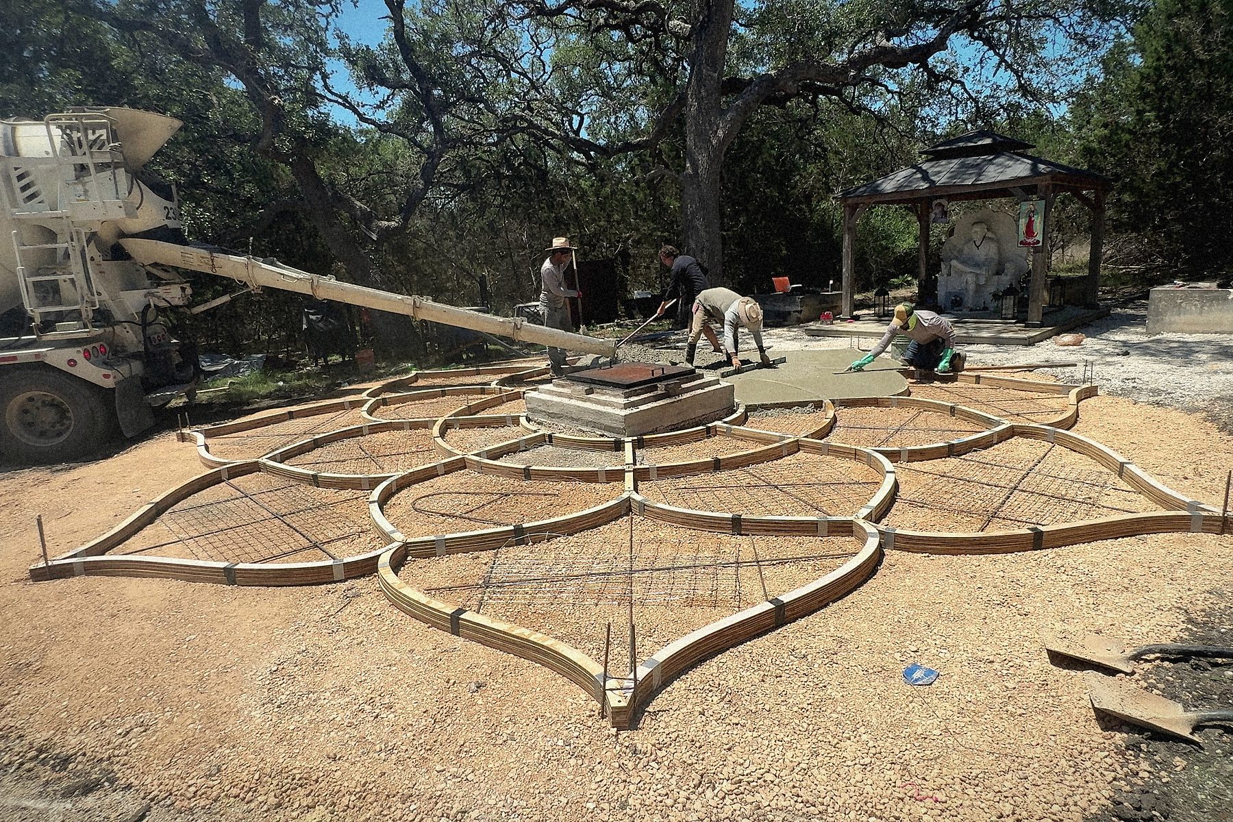 Pour day at ground level: the chute over the forms, the crew at the plinth, the shrine behind.
